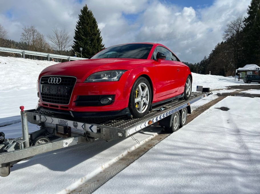 Professionelle Fahrzeugüberführung – Sicher ans Ziel Sicherer Fahrzeugtransport eines roten Audi TT auf einem Spezialanhänger während des Winters.